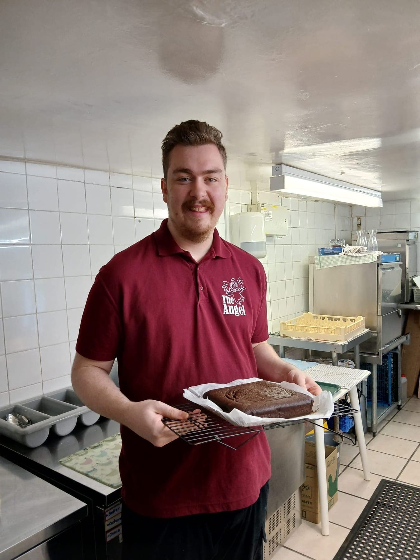 A team member in Angel uniform holding a freshly baked chocolate cake in the kitchen